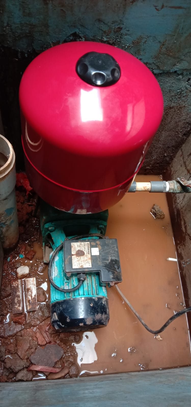 Servis pompa booster dengan pressure tank merah di dalam bak pompa yang tergenang